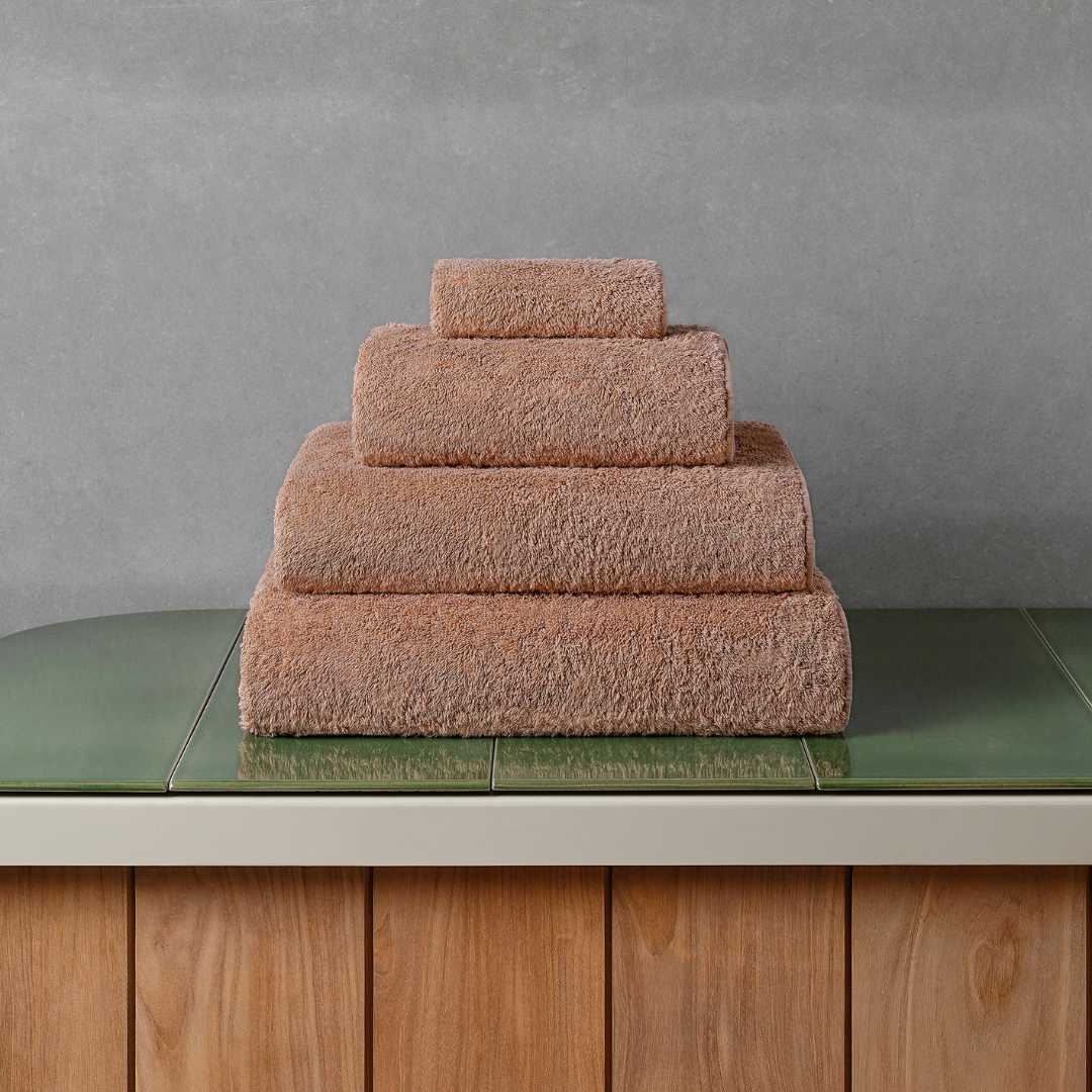 Stack of cinnamon bath towels on a green tiled bathroom counter