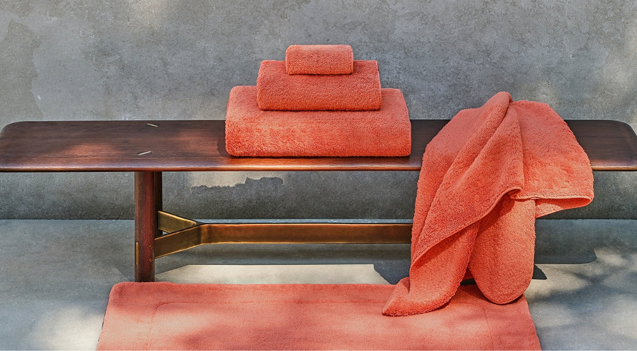Orange towels on a wooden bench against a gray wall.