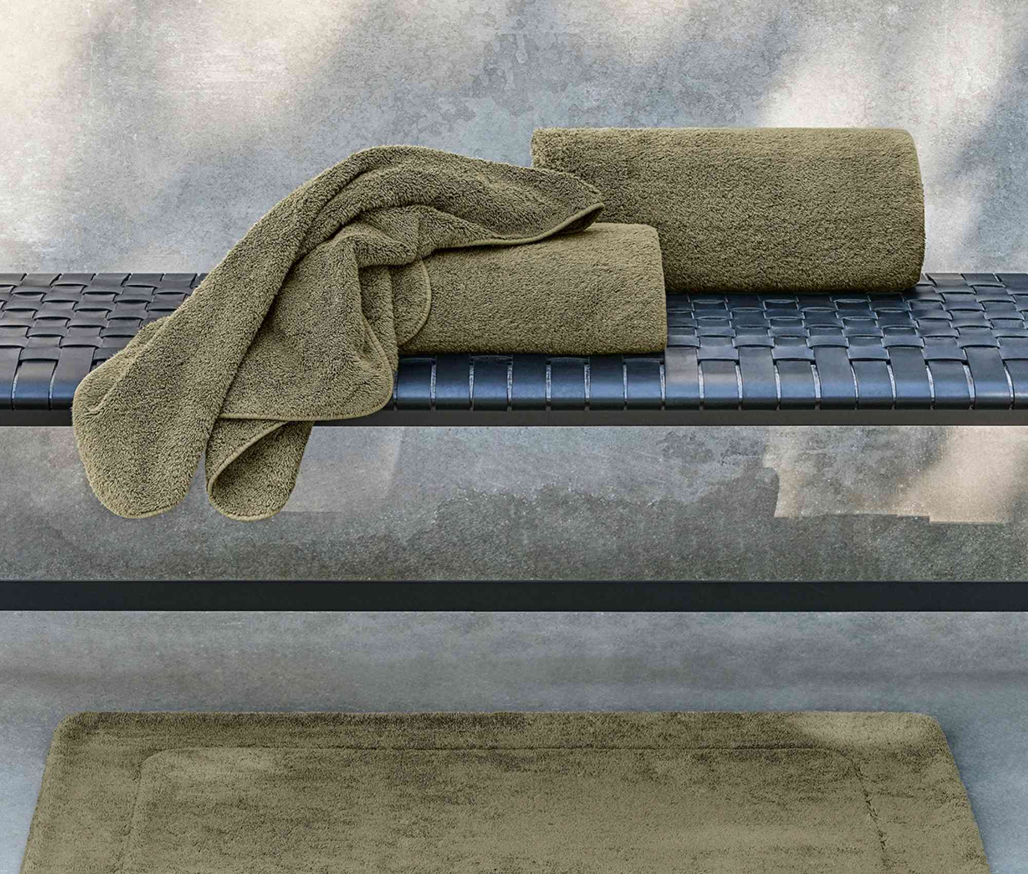 Green bath towels on a metal surface with a concrete wall background