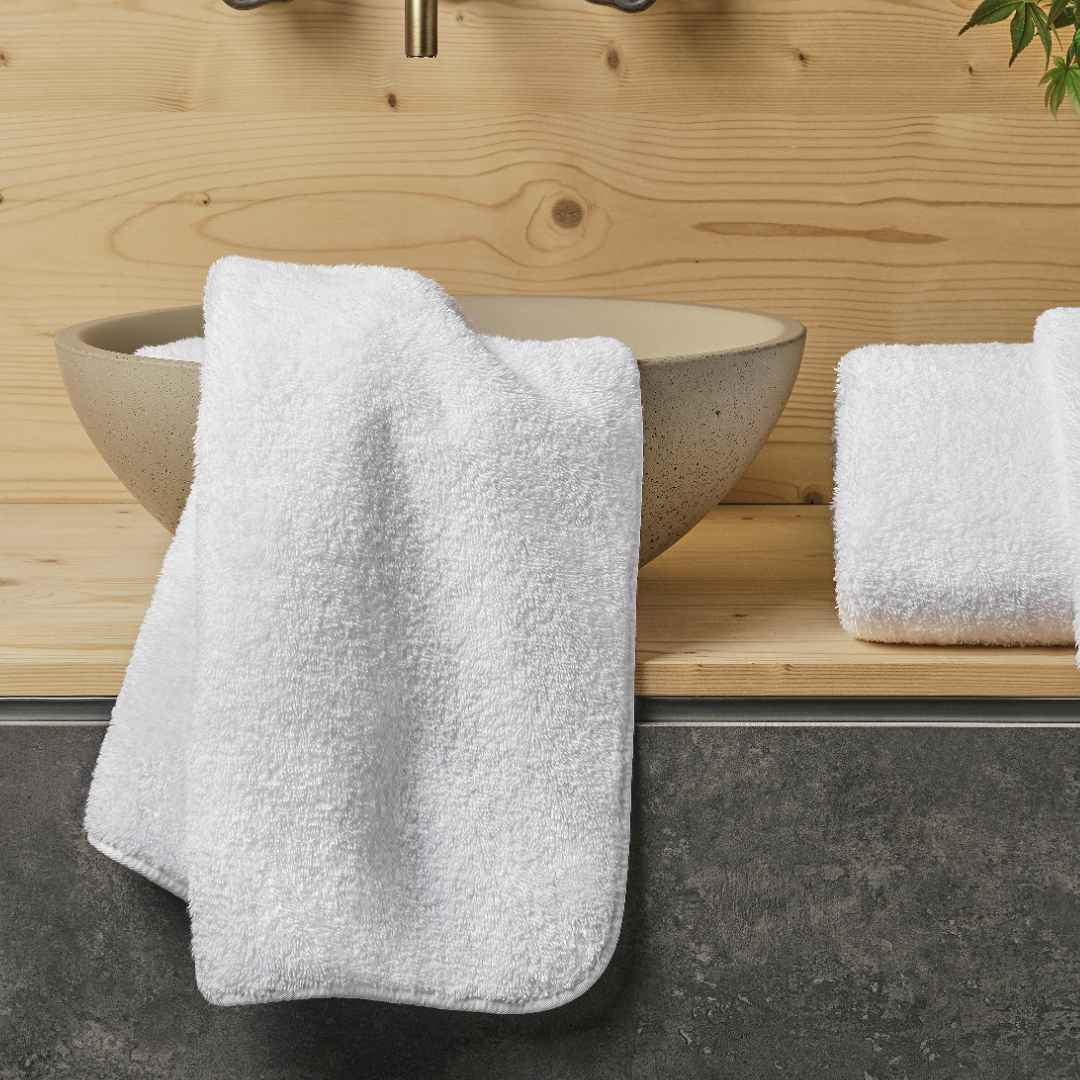 White bath towels beside a ceramic sink on a wooden bathroom counter