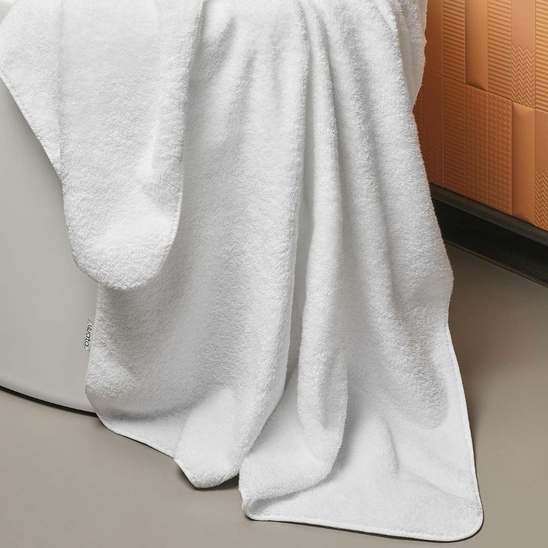 White towel draped over a bathtub with a textured wall in the background.